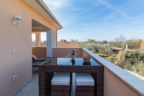 A balcony with a glass-top table, wicker furniture, and a view of the surrounding landscape.