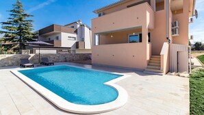 Una moderna casa a due piani con piscina, un muro in pietra e un prato curato.