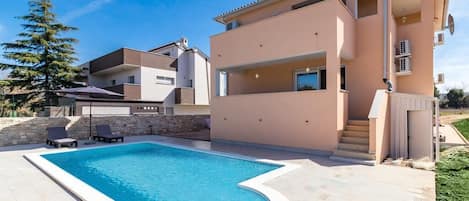 Uma casa moderna com dois andares, piscina, muro de pedra e gramado bem cuidado.