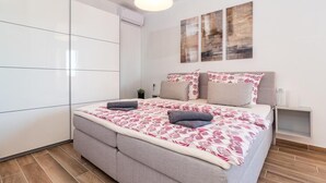 Una camera da letto moderna con un letto grande, una testiera grigia imbottita e un armadio bianco.