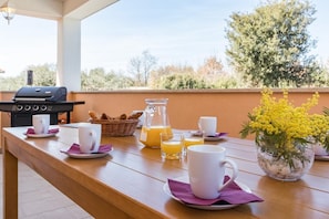 A breakfast setup with a grill, coffee cups, juice, and a flower vase on a wooden table.