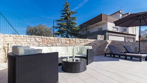 Una terrazza esterna con mobili in vimini, un muro in pietra e vista su un edificio moderno.
