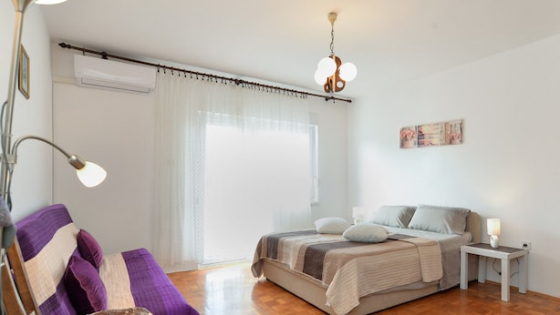 A bedroom with a bed, a bedside table, a lamp, a chair, and a window with curtains. - Apartment 1822 (Pula)