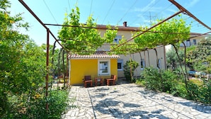 A yellow building with a tiled roof, a stone patio, and a pergola with vines. - Apartment 1822 (Pula)