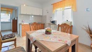 A compact kitchen with white cabinets, a microwave, and a dining table with chairs. - Apartment 1822 (Pula)