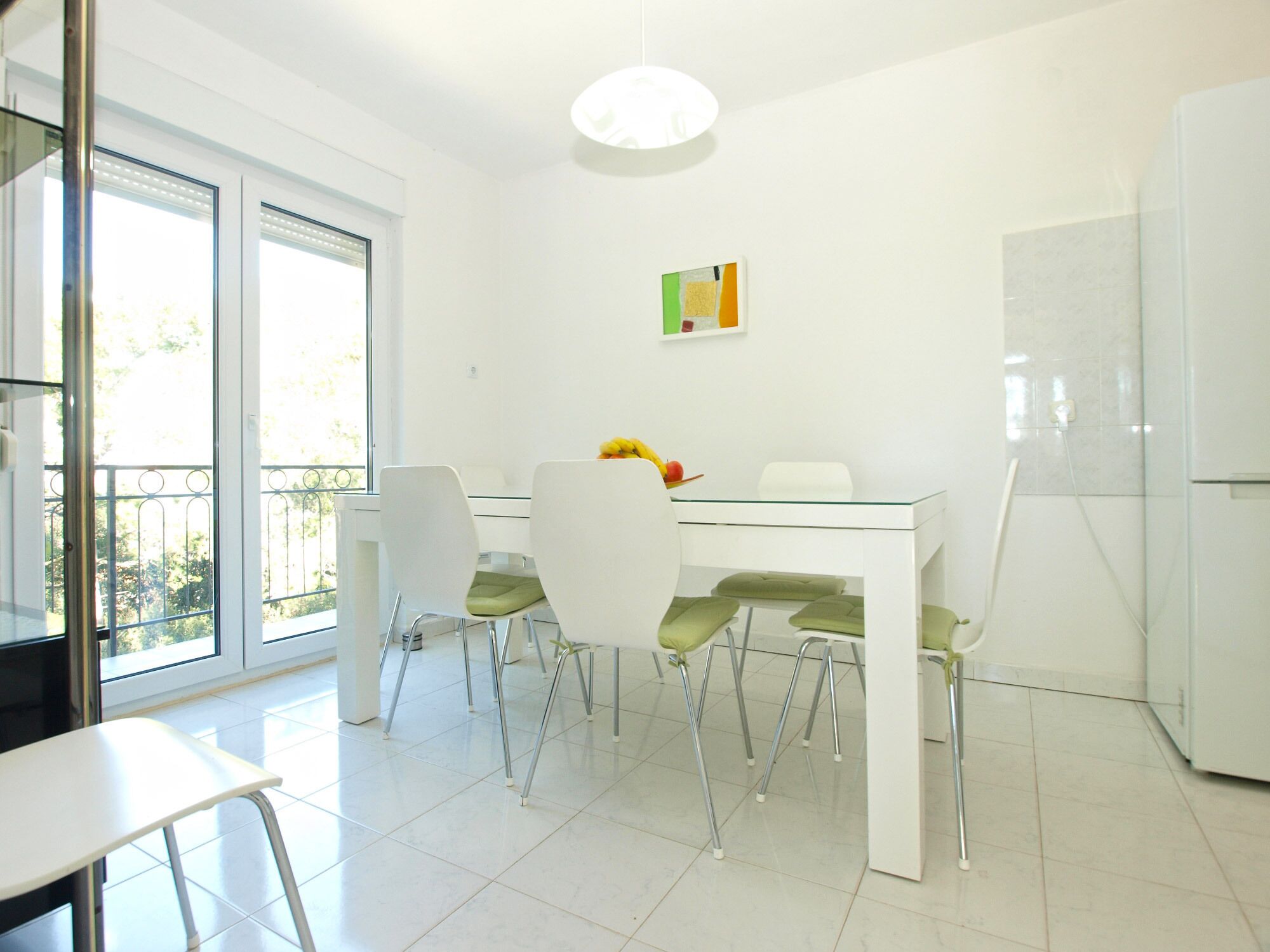 Une cuisine moderne avec des meubles blancs, une table à manger en verre et quatre chaises.