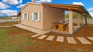 Ein kleines, eingeschossiges Haus mit Terrasse, Schornstein und Blick auf die umliegende Landschaft.