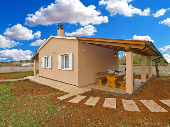 Ein kleines, eingeschossiges Haus mit Terrasse, Schornstein und Blick auf die umliegende Landschaft.