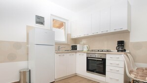 Eine kompakte Küche mit weißen Schränken, einem eingebauten Backofen, einer Mikrowelle und einer Kaffeemaschine.
