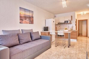 Cozy living space with a sofa, two chairs, and a kitchen area, featuring a painting of a beach scene.