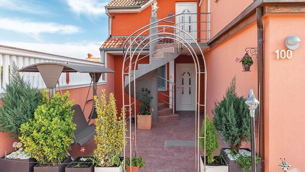 Un immeuble à la façade rouge, avec un escalier en métal et une porte numérotée 100.