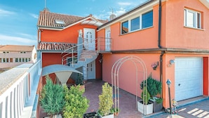 Une maison à deux étages avec une façade rouge, une porte de garage blanche et un petit jardin agrémenté de plantes en pot.