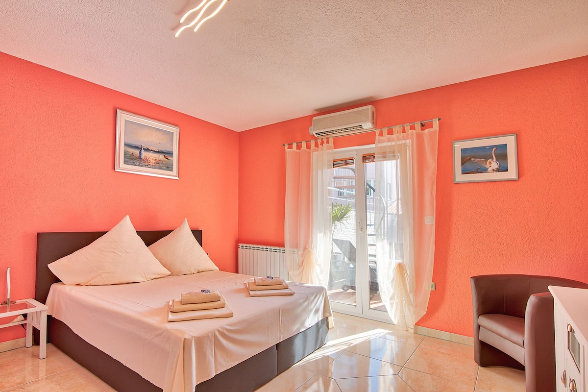 A hotel room with a bed, a chair, a table, and a window with curtains.