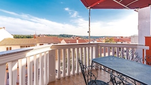 Un balcon avec une table et des chaises, des balustrades blanches et un auvent rouge.