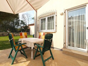 Un patio al aire libre con mesa y sillas, una zona cubierta, una ventana con rejas y una puerta corrediza de vidrio.