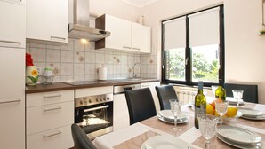A modern kitchen with white cabinets, a built-in oven, and a dining area set for four with a table, chairs, and wine glasses. - Apartment 1844 (Pula)
