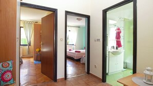 A hotel room with a wooden floor, a bed with a pink bedspread, a bathroom with a sink and a mirror, and a small table with a decorative item. - Apartment 1844 (Pula)