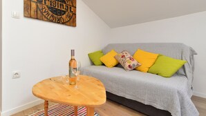 Ett mysigt vardagsrum med en grå soffa, färgglada kuddar, ett träbord och en vinflaska.
