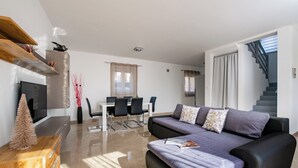 A modern living room with a sofa, a coffee table, a TV, and a dining area with chairs and a table. - House 1855 (Liznjan)