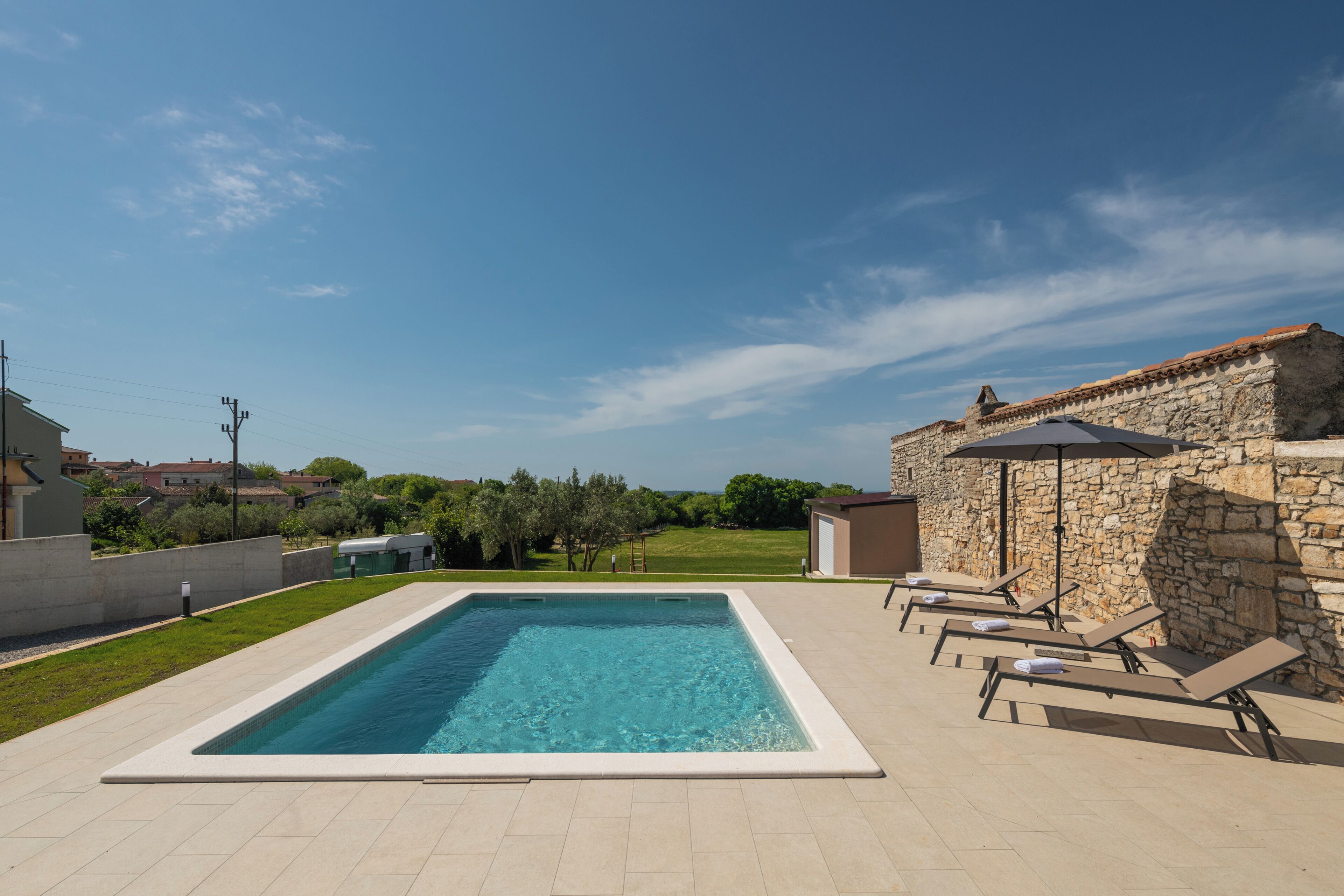 A rectangular swimming pool with a stone wall and lounge chairs on one side.