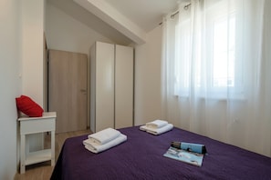 Un dormitorio con una colcha morada, dos toallas ordenadamente dobladas, una almohada roja y una revista sobre la cama.