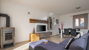 A modern living room with a sofa, flat-screen TV, fireplace, wooden cabinet, and dining area. - House 1855 (Liznjan)