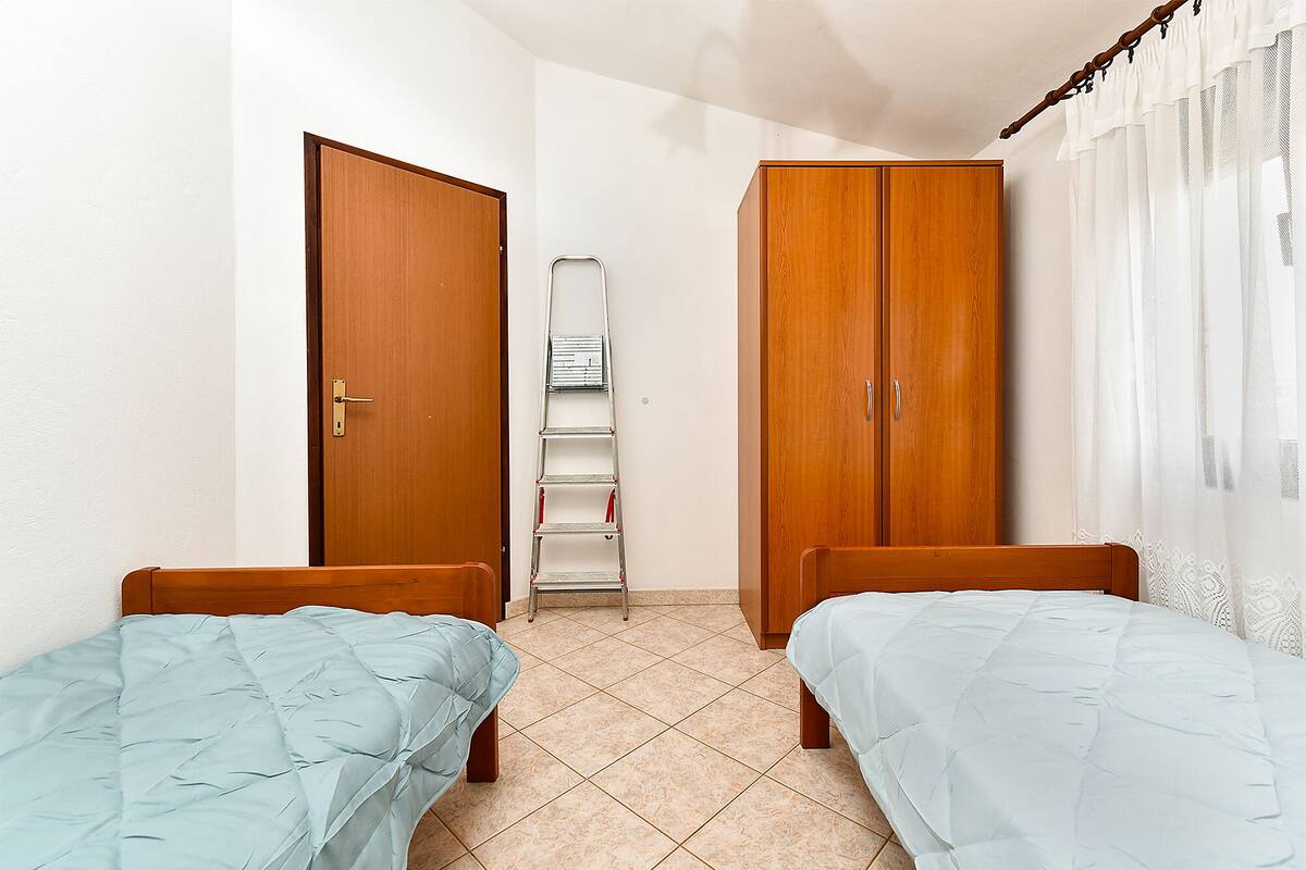 A bedroom with two wooden beds, a wardrobe, and a ladder against the wall.