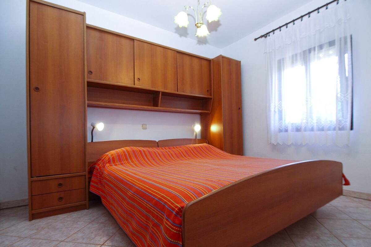 A bedroom with a wooden bed frame, a built-in wardrobe, and a window with curtains.