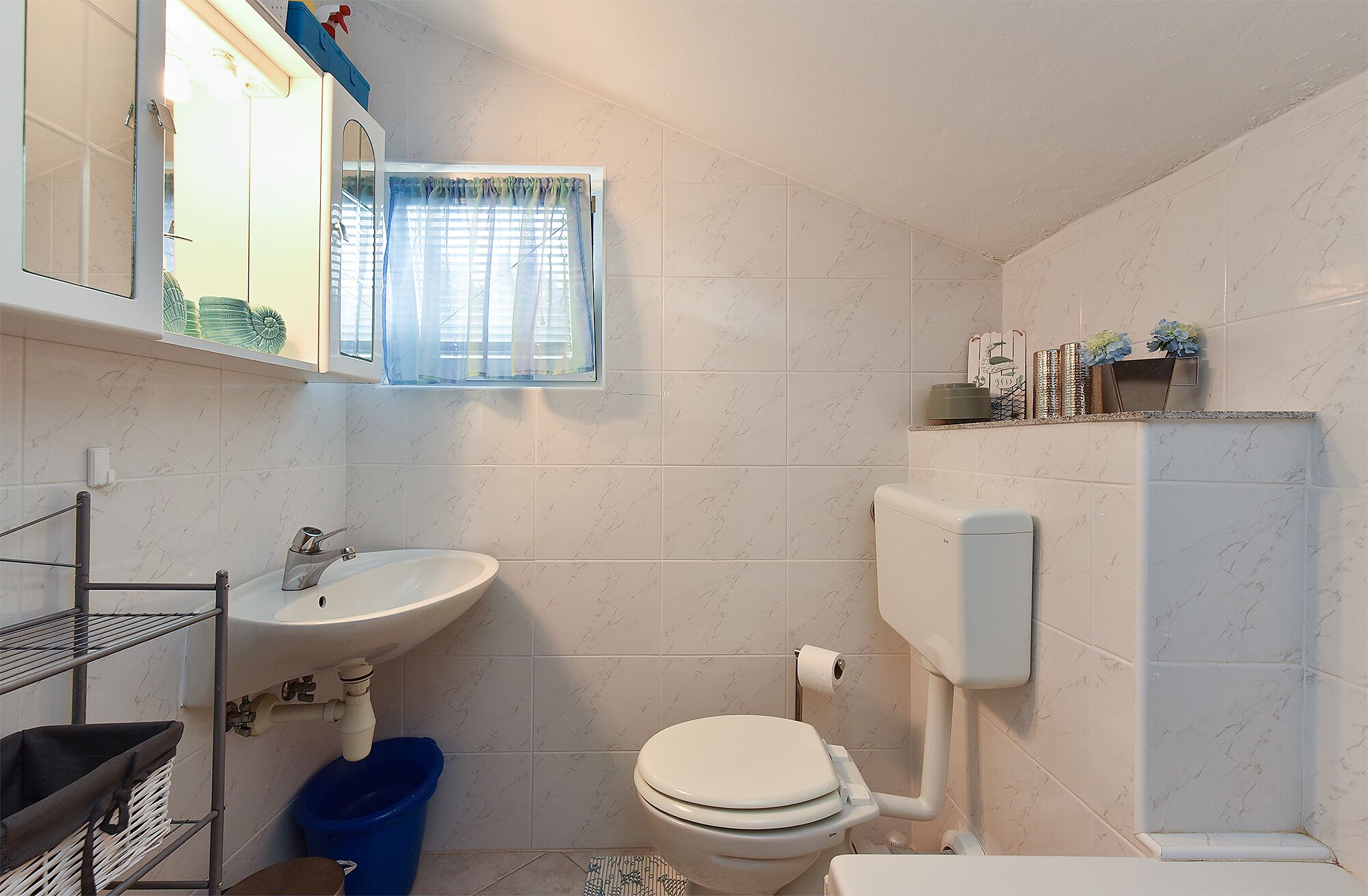 A compact bathroom with a white sink, toilet, and a window with blue curtains.