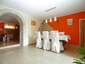 A dining area with a stone archway, a table set for four with white chairs, and a bright orange wall. - Apartment 1862 (Zminj)