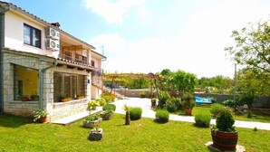 A two-story house with a stone facade, a balcony, and a garden with various potted plants and a small lawn. - Apartment 1862 (Zminj)