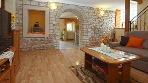 A living room with a stone wall, wooden furniture, a sofa, and a television. - Apartment 1862 (Zminj)
