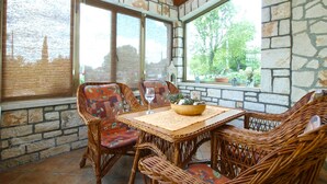 A covered patio with wicker furniture, stone walls, and large windows overlooking a garden. - Apartment 1862 (Zminj)