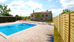 A swimming pool with lounge chairs, a stone house, and a wooden fence in a sunny backyard. - Apartment 1862 (Zminj)
