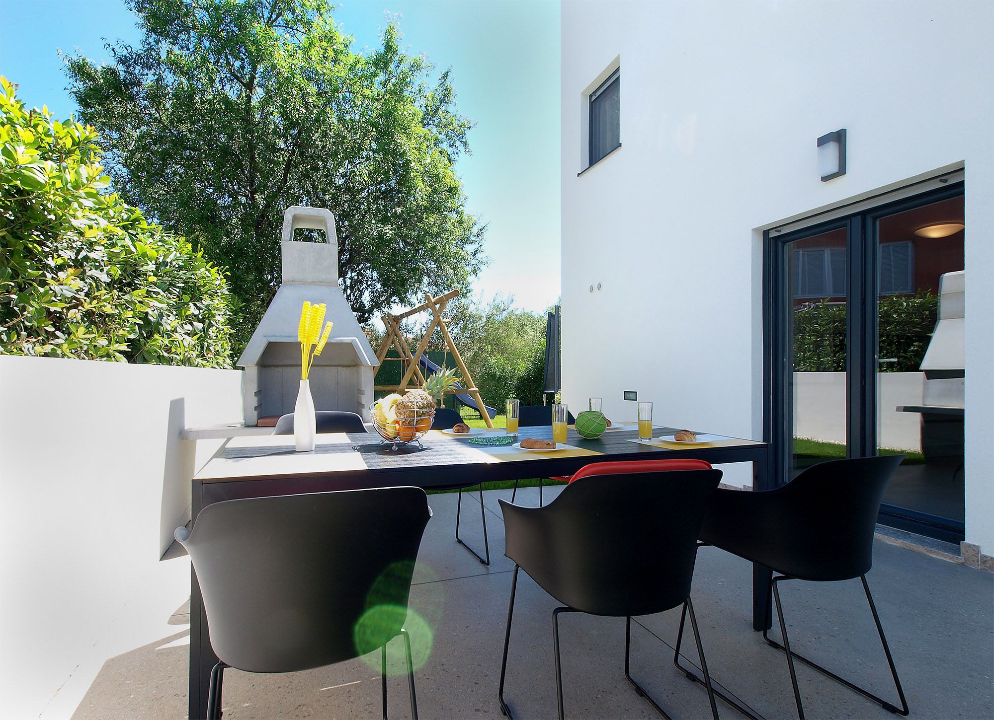 An outdoor dining area with a grill, chairs, and a table set for a meal.