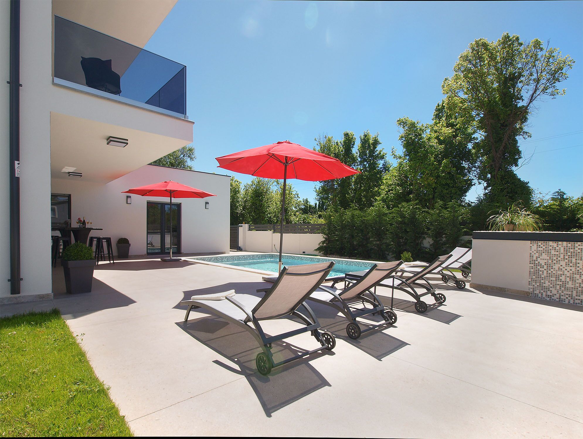 Ein moderner Poolbereich im Freien mit Liegestühlen und roten Sonnenschirmen.