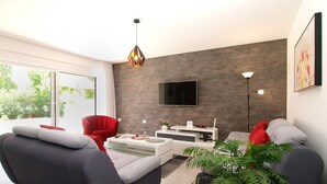 Ein modernes Wohnzimmer mit grauem Sofa, rotem Sessel und einem flachbildfernseher, der an einer strukturierten Wand angebracht ist.