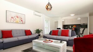Ein modernes Wohnzimmer mit zwei grauen Sofas, einem Glastisch und einem roten Sessel.