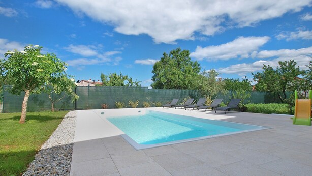 A rectangular swimming pool with a tiled deck, surrounded by a low stone wall and a green fence. - Apartment 1868 (Pula)