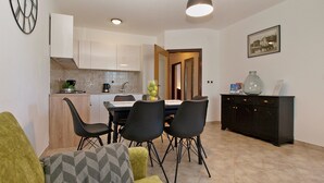 A modern kitchen with white cabinets, a dining area with a table and chairs, and a living space with a sofa and cushions. - Apartment 1868 (Pula)