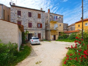 A narrow street with a white car parked on the side, flanked by stone and painted buildings with multiple windows and balconies. - Apartment 1872 (Fazana)