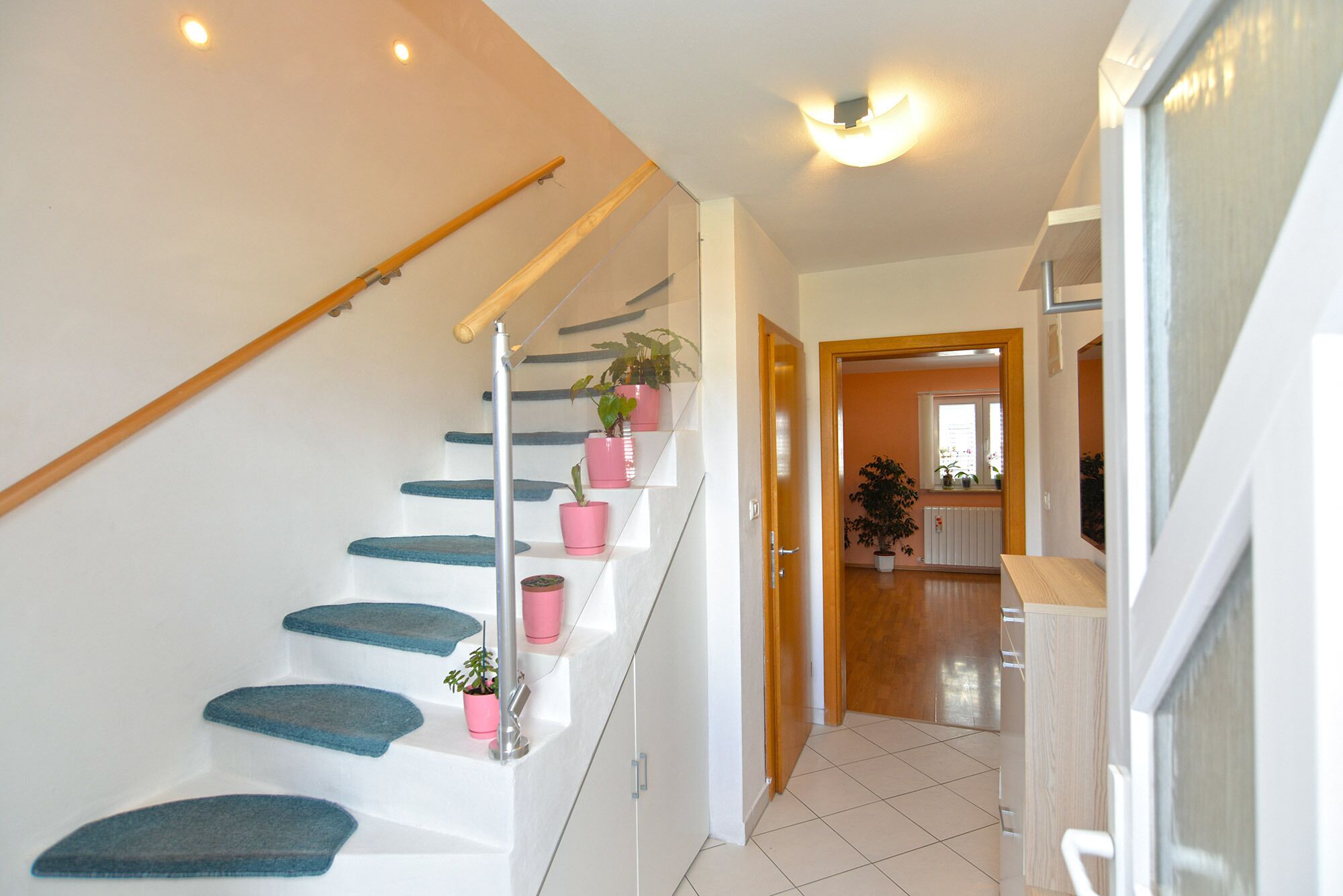 A staircase with blue steps and pink planters, leading to a room with a wooden door and a window.