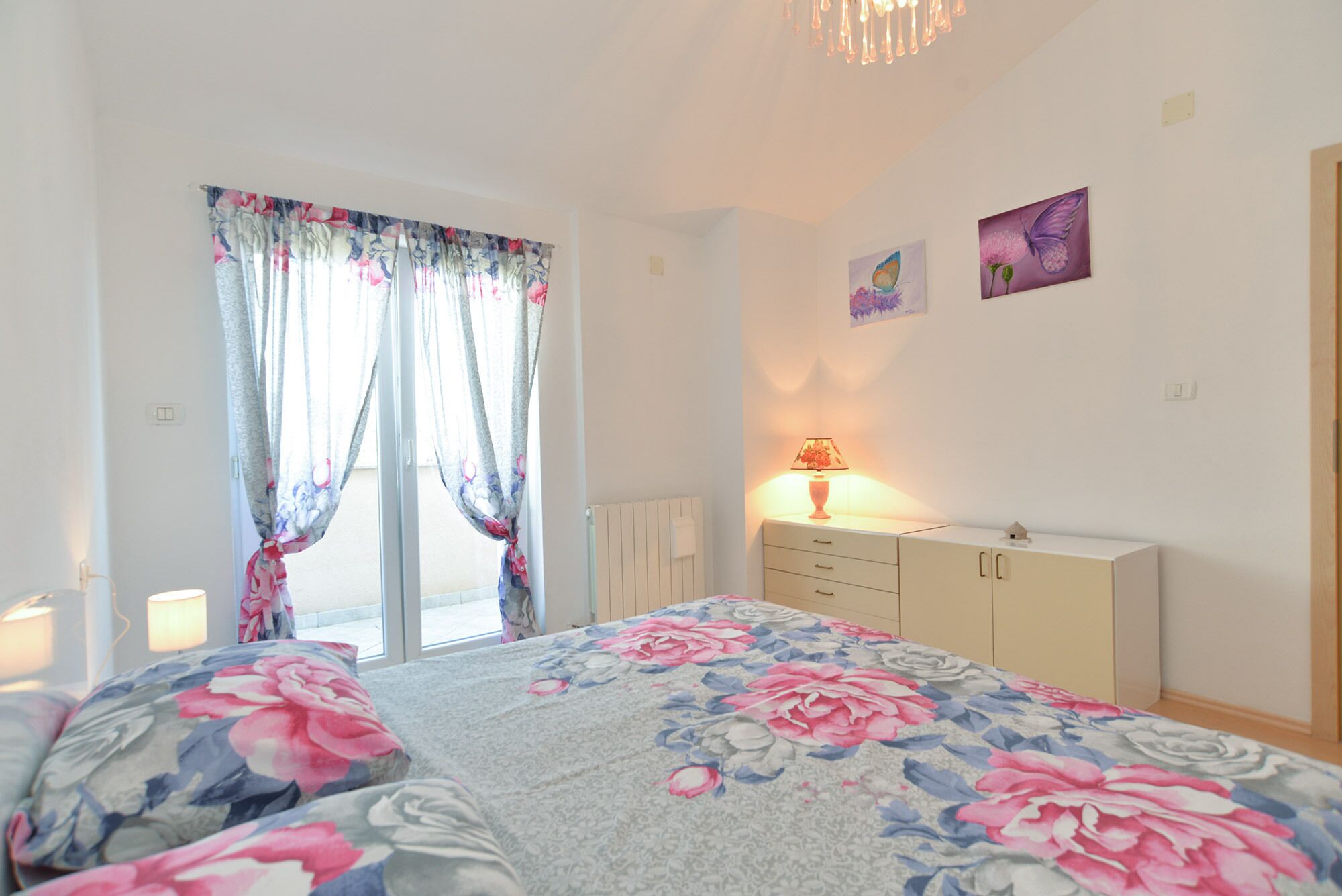 A bedroom with a bed, a nightstand, a dresser, and a window with curtains.