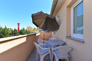 Ein Balkon mit Tisch, Stühlen und Sonnenschirm, mit Blick auf Gebäude im Hintergrund.