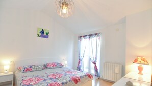 A bedroom with a bed, a nightstand, a lamp, a radiator, and a window with floral curtains. - Apartment 1873 (Pula)