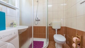 Un baño con cabina de ducha de vidrio, inodoro blanco, lavamanos y lavadora.