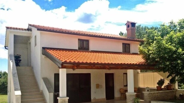 Una casa de dos pisos con techo de tejas, un porche cubierto y una escalera que conduce al segundo piso.