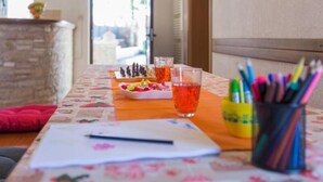 Una mesa con mantel floral, un tablero de ajedrez, un vaso de bebida roja y una taza de bolígrafos.