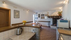 Una cocina con encimera de piedra, una tetera y una estufa. Hay una puerta de madera y un cuadro en la pared.
