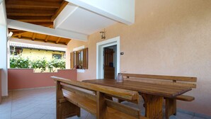A wooden table and benches in a covered outdoor area with a tiled floor and a beige wall. - Apartment 1875 (Marcana)